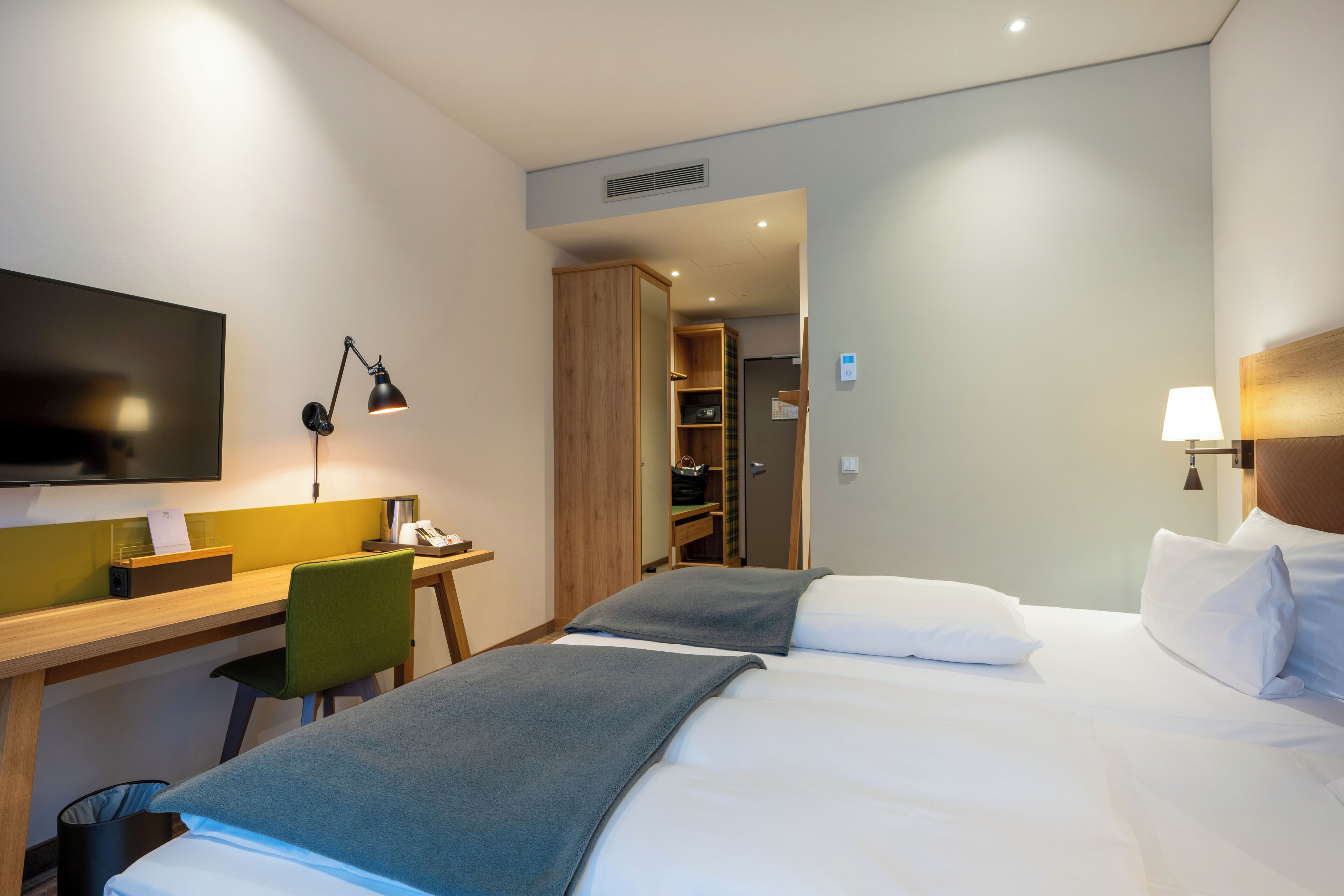 A hotel room with a bed, a desk, a chair, a TV, and a wardrobe.