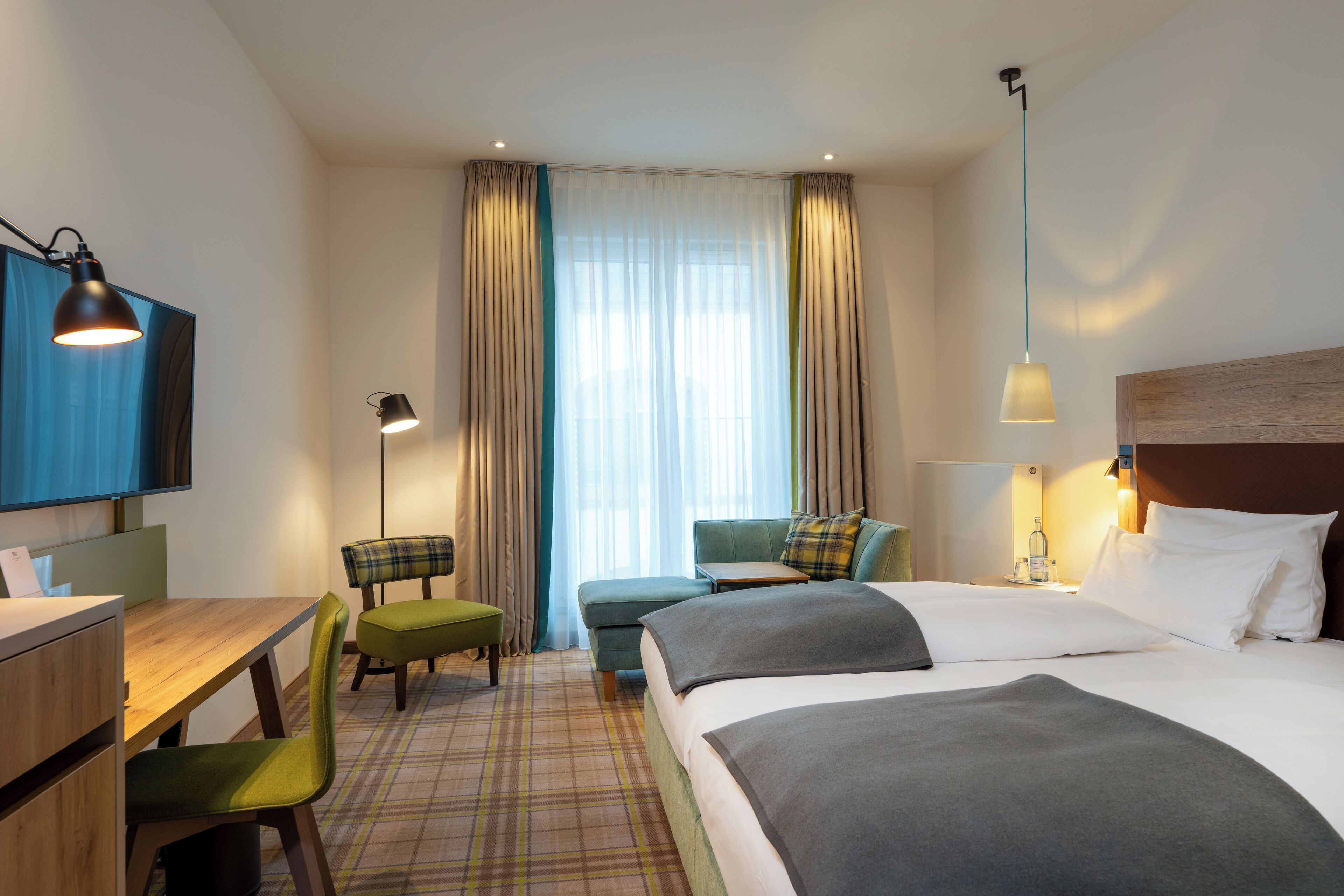 A hotel room with a bed, a desk, a chair, a sofa, and a television.