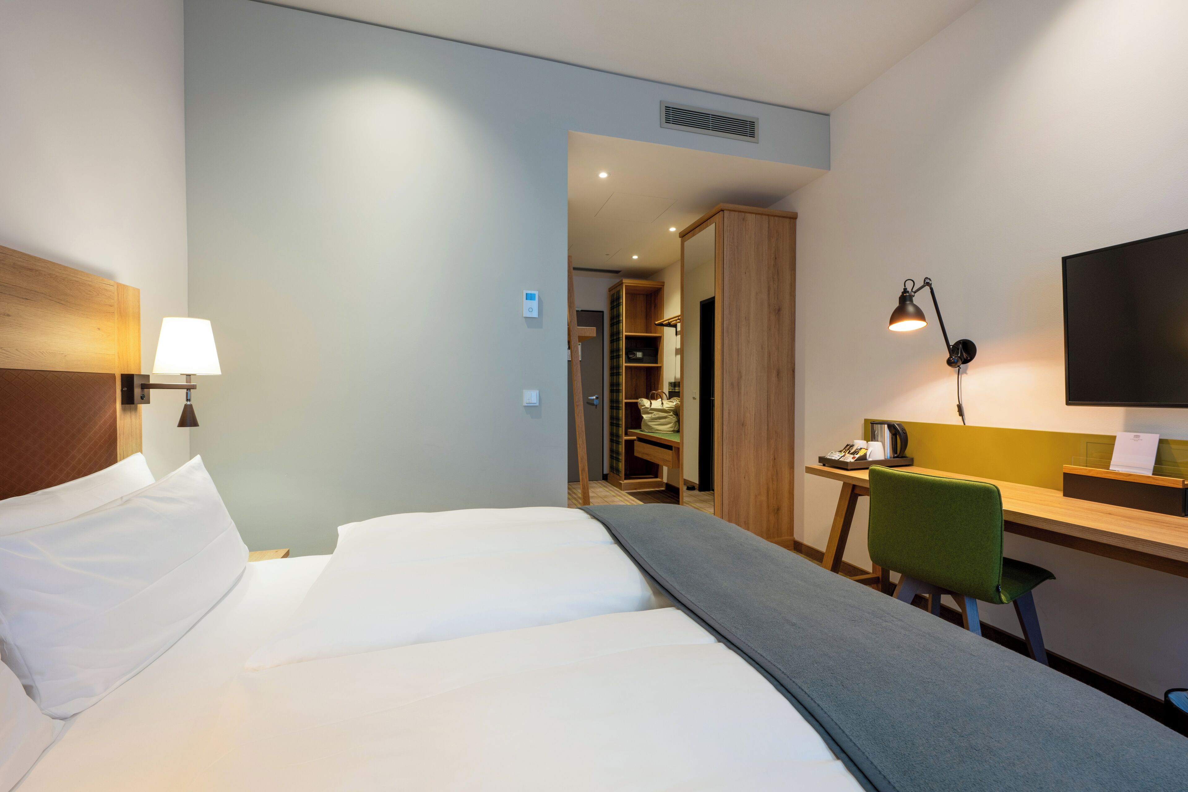 Une chambre d’hôtel équipée d’un lit, d’un bureau, d’une chaise, d’une lampe et d’un téléviseur fixé au mur.