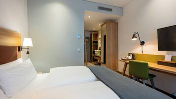 Une chambre d’hôtel équipée d’un lit, d’un bureau, d’une chaise, d’une lampe et d’un téléviseur fixé au mur.