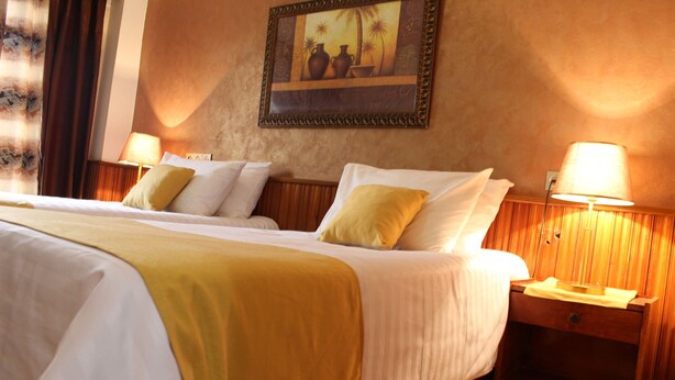 A hotel room with a large bed, two bedside tables with lamps, a painting on the wall, and a wooden floor.