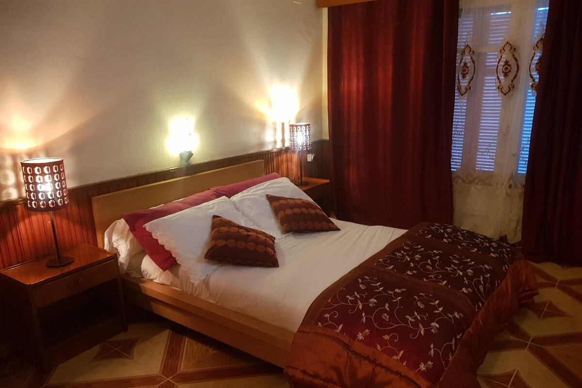 A neatly made bed with a patterned bedspread, two bedside lamps, and a decorative wall lamp.