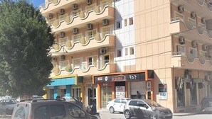 A multi-story building with balconies, a storefront, and parked cars.