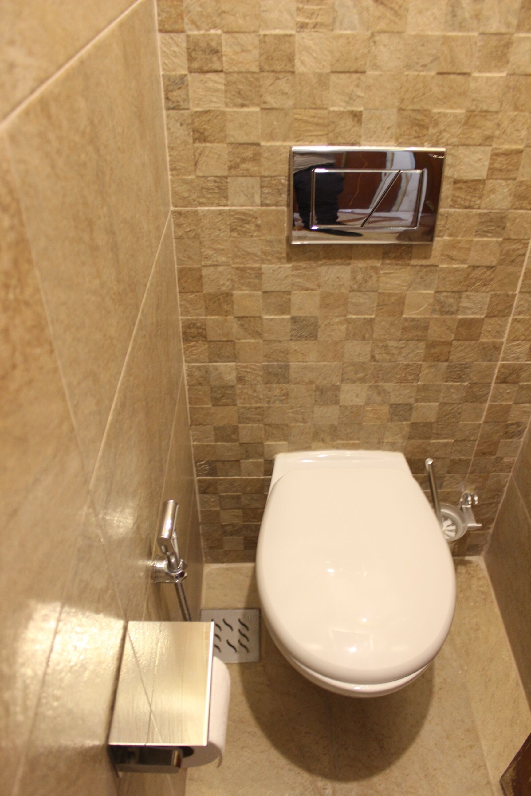 Baño con inodoro, secador de manos y un cesto de basura. Las paredes están cubiertas con un patrón de mosaicos en blanco y negro.