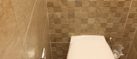 Baño con inodoro, secador de manos y un cesto de basura. Las paredes están cubiertas con un patrón de mosaicos en blanco y negro.