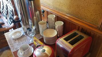Une petite cuisine équipée d’une machine à café, d’un grille-pain, ainsi que d’une pile de tasses et d’assiettes.