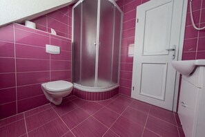A bathroom with pink tiles, a white toilet, a shower enclosure, and a white sink. - Villa Lika Annex (Plitvicka Jezera)