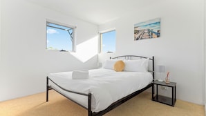 Ein Schlafzimmer mit einem Bett, zwei Fenstern, einem Nachttisch und einem Bild an der Wand.