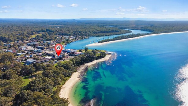 Luftaufnahme einer Küstenstadt mit Strand, klarem blauen Wasser und einem dichten Waldgebiet.