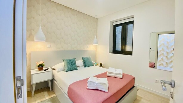 A modern bedroom with a large bed, a nightstand, a bedside table, a window, and a mirror.
