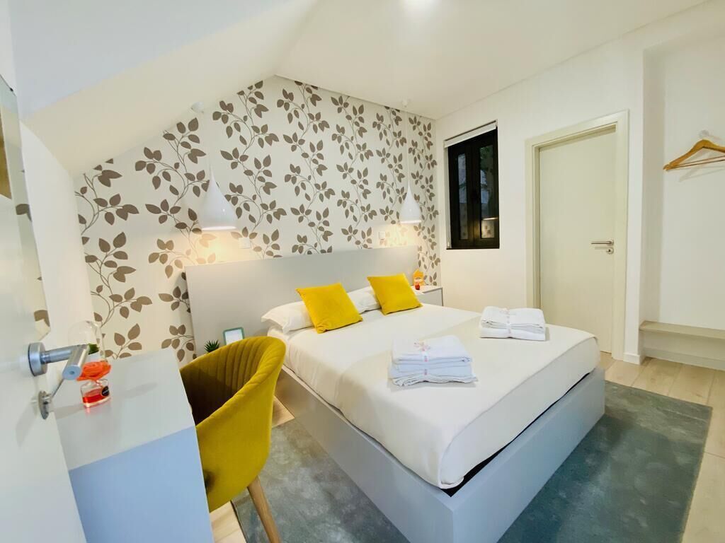 A modern bedroom with a large bed, a desk, and a chair. There is a window with a view of the outside.