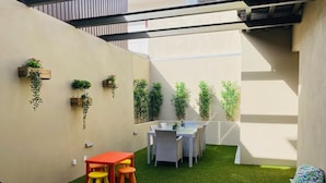 A small outdoor area with a table and chairs, artificial grass, and potted plants on the walls.