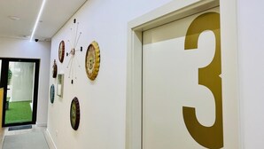 A hallway with a door marked with the number 3, a glass door leading outside, and wall-mounted clocks.