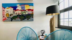 A room with two blue chairs, a painting of colorful buildings, a lamp, and a globe on a small table.