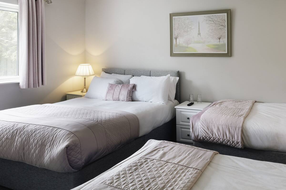 A hotel room with two beds, a nightstand with a lamp, a bedside table, and a framed picture on the wall.