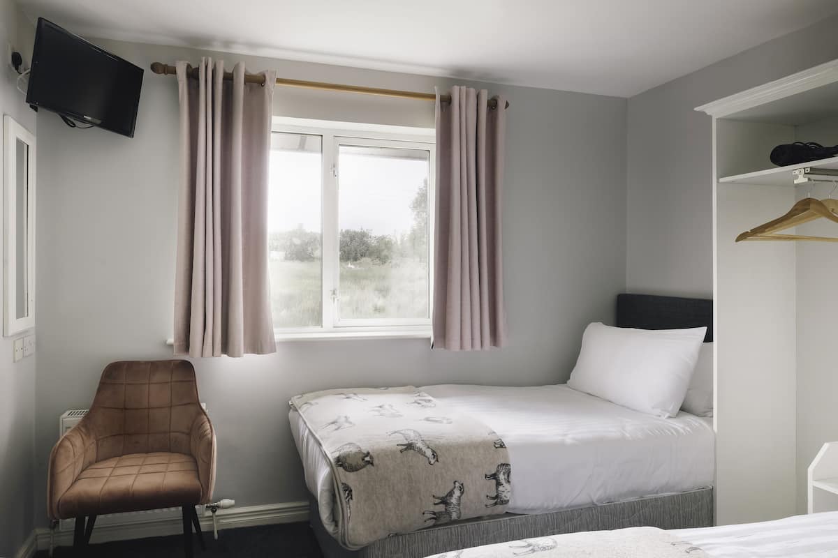 A bedroom with a bed, a chair, a TV, and a window with curtains.