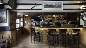 A bar area with wooden bar stools, a counter with various bottles, and a framed picture on the wall. - The Climbers Inn (Glencar)
