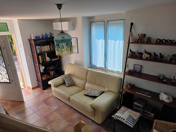 Ein Wohnzimmer mit einem beigen Sofa, einem Bücherregal, einer Hängelampe und einem Fenster mit Vorhängen.