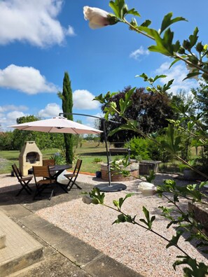 Ein Außenbereich mit Terrasse, Grill, Sitzgelegenheiten und einer Pergola mit Sonnenschirm.