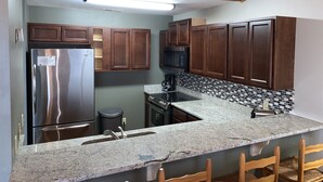 A kitchen with wooden cabinets, a stainless steel refrigerator, a microwave, and a granite countertop. - Oceanfront Escape at Eastern Sails (North Topsail Beach)