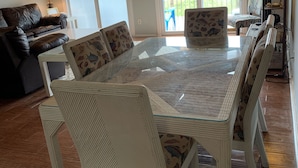 A dining area with a round table and white chairs, a ceiling fan, and a view of the outdoors through large sliding doors. - Oceanfront Escape at Eastern Sails (North Topsail Beach)