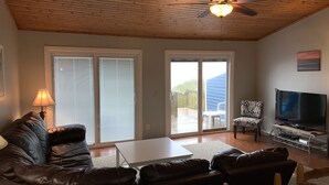 A living room with a leather sofa, a coffee table, a TV, and a ceiling fan. - Oceanfront Escape at Eastern Sails (North Topsail Beach)