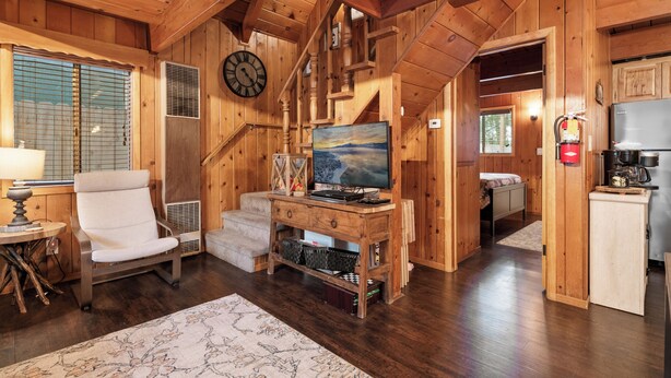 A wooden cabin interior with a living area featuring a TV, a chair, a small table, and a fireplace.