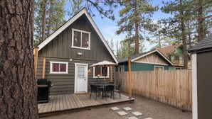 A two-story cabin with a deck, a patio with outdoor furniture, and a wooden fence.