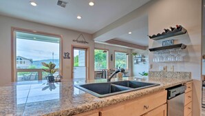 A modern kitchen with a granite countertop, stainless steel sink, and wooden cabinets. There is a wine rack above the sink and a dining area visible through the open door. - Lake Chelan Home in Private Community w/ Lake View (Manson)