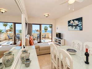 A modern living room with a sofa, dining table, and chairs, a TV, and a painting of flowers. - 1162 Apartment Burriana (Nerja)