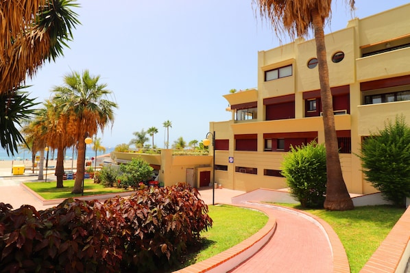 Un hotel de varios pisos con diseño moderno, que cuenta con balcones, un patio central y palmeras.