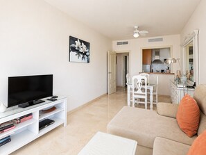 A living room with a flat-screen TV, a glass coffee table, a beige sofa, and a dining area with a white chair. - 1162 Apartment Burriana (Nerja)