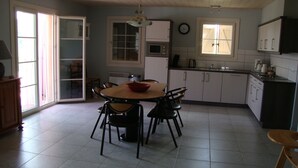 A kitchen with a dining table, chairs, cabinets, a clock, and a window. - Beautiful newly built house with private pool in the Ardèche (Chassagnes)