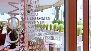 A view through a glass door of a hotel lobby with a balcony, potted plants, and outdoor seating. - Park Hotel Pineta (Caorle)