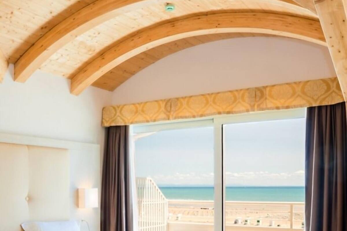 A bedroom with a bed, bench, and a large window offering a view of the beach.