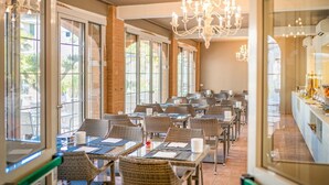 A restaurant with wicker chairs and tables, large windows, and a chandelier. - Park Hotel Pineta (Caorle)
