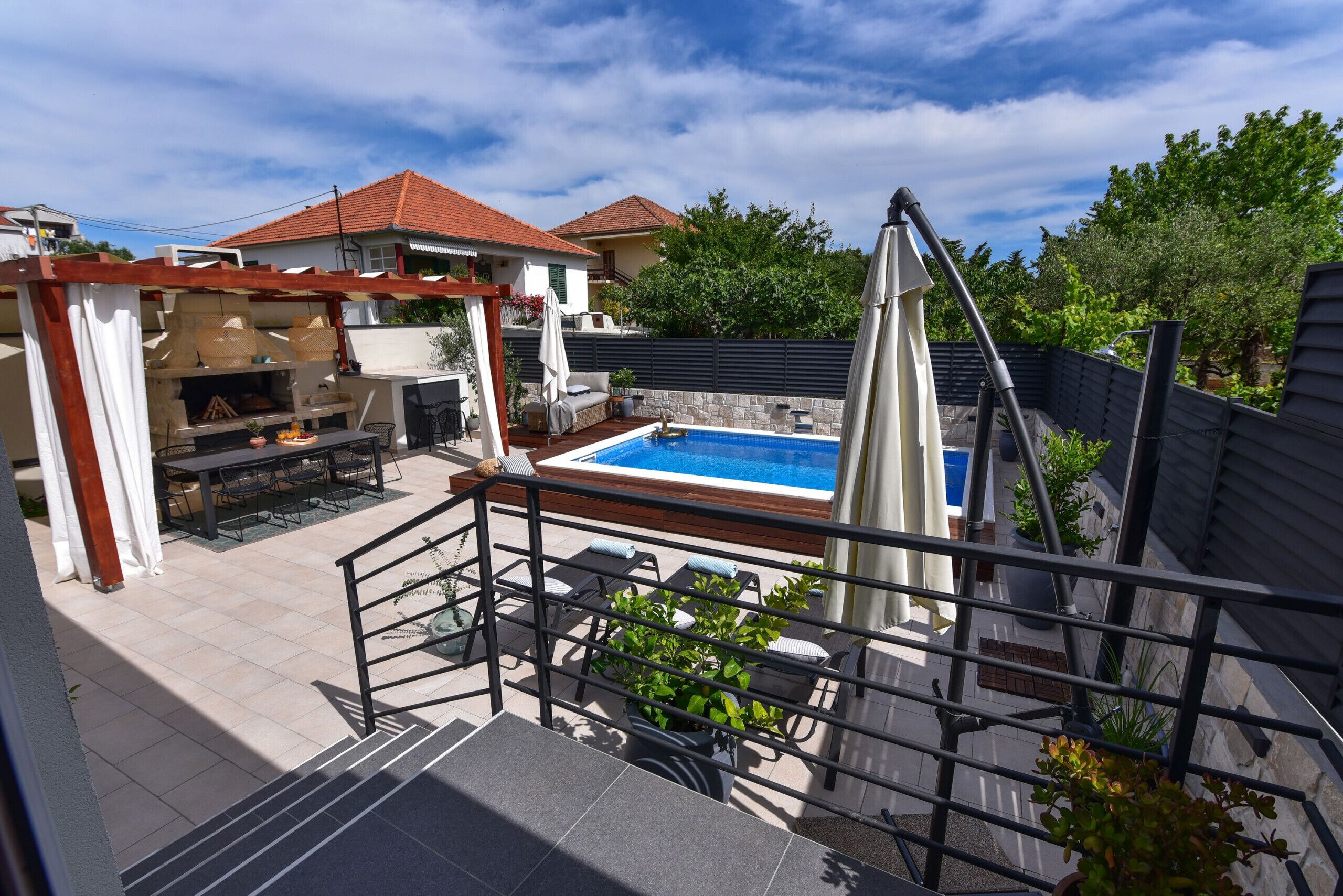 A rooftop pool area with a pergola, outdoor seating, and a view of neighboring houses.