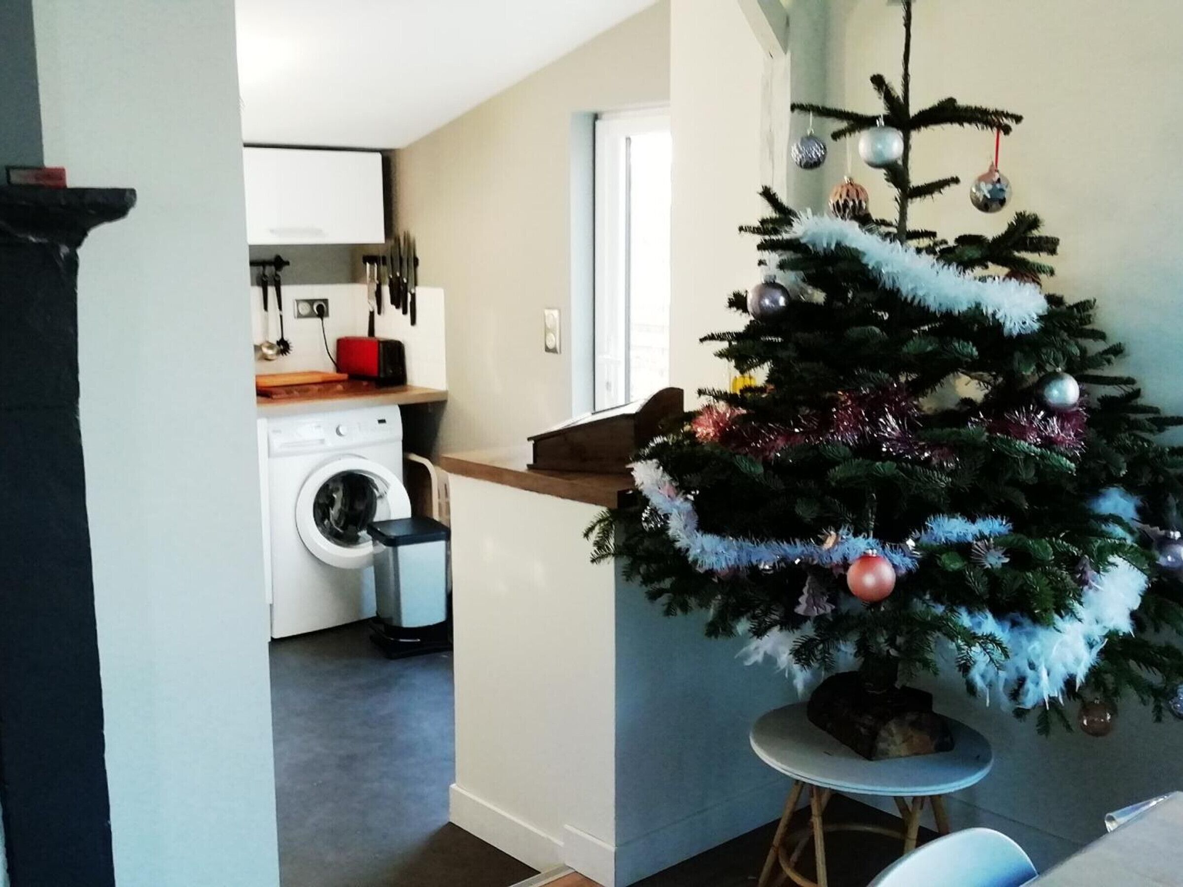 A modern kitchen with a washing machine, a dining area with a small table, and a Christmas tree.