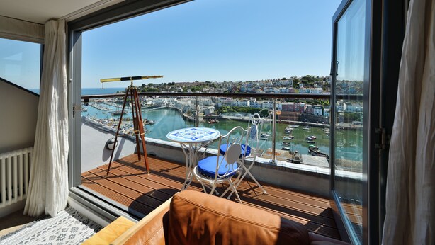 A balcony with a table and chairs, a view of a marina, and a cityscape in the background. - Beacon House (Brixham)