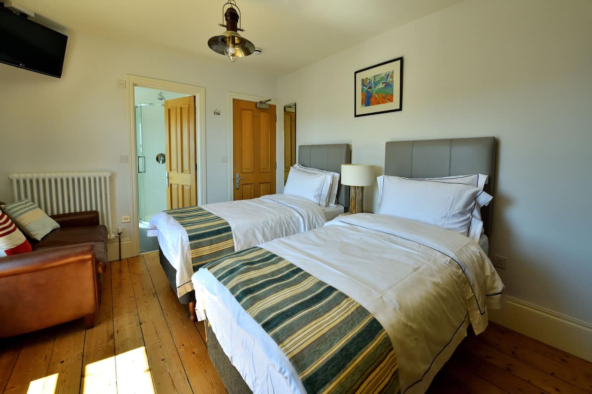 A hotel room with two beds, a wooden floor, a radiator, a television, and a door leading to another room.