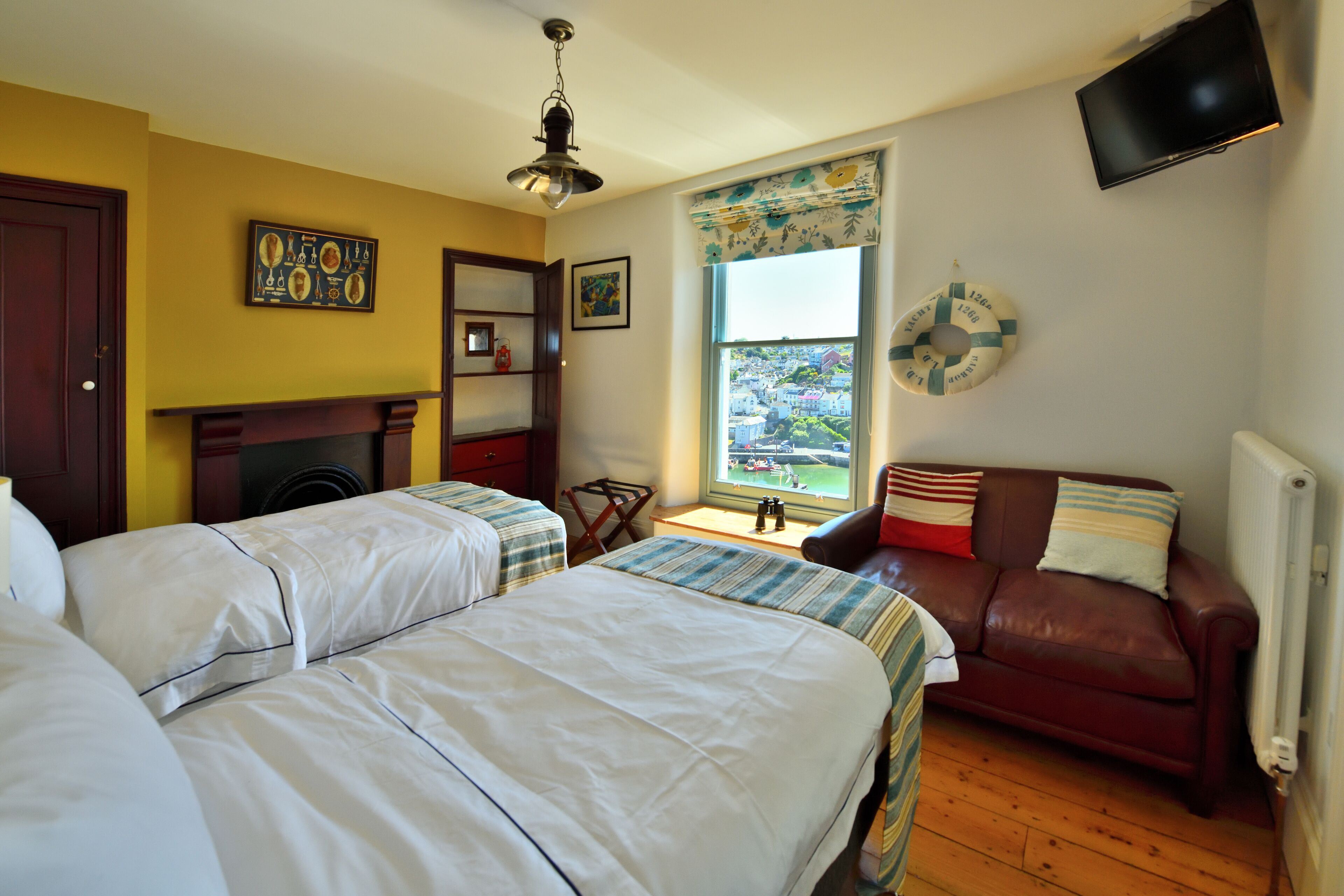 A hotel room with two beds, a fireplace, a television, and a window with a view of a town.