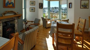 A cozy living room with a fireplace, striped chairs, a dining table, and a bay window with a view of the town. - Beacon House (Brixham)
