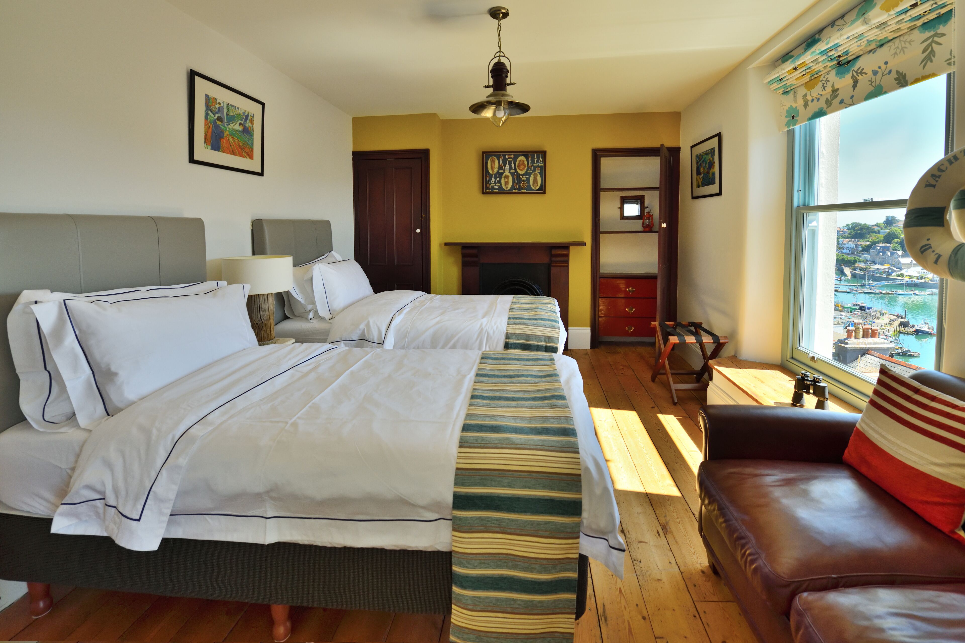 A hotel room with two beds, a sofa, a fireplace, and a view of the harbor.