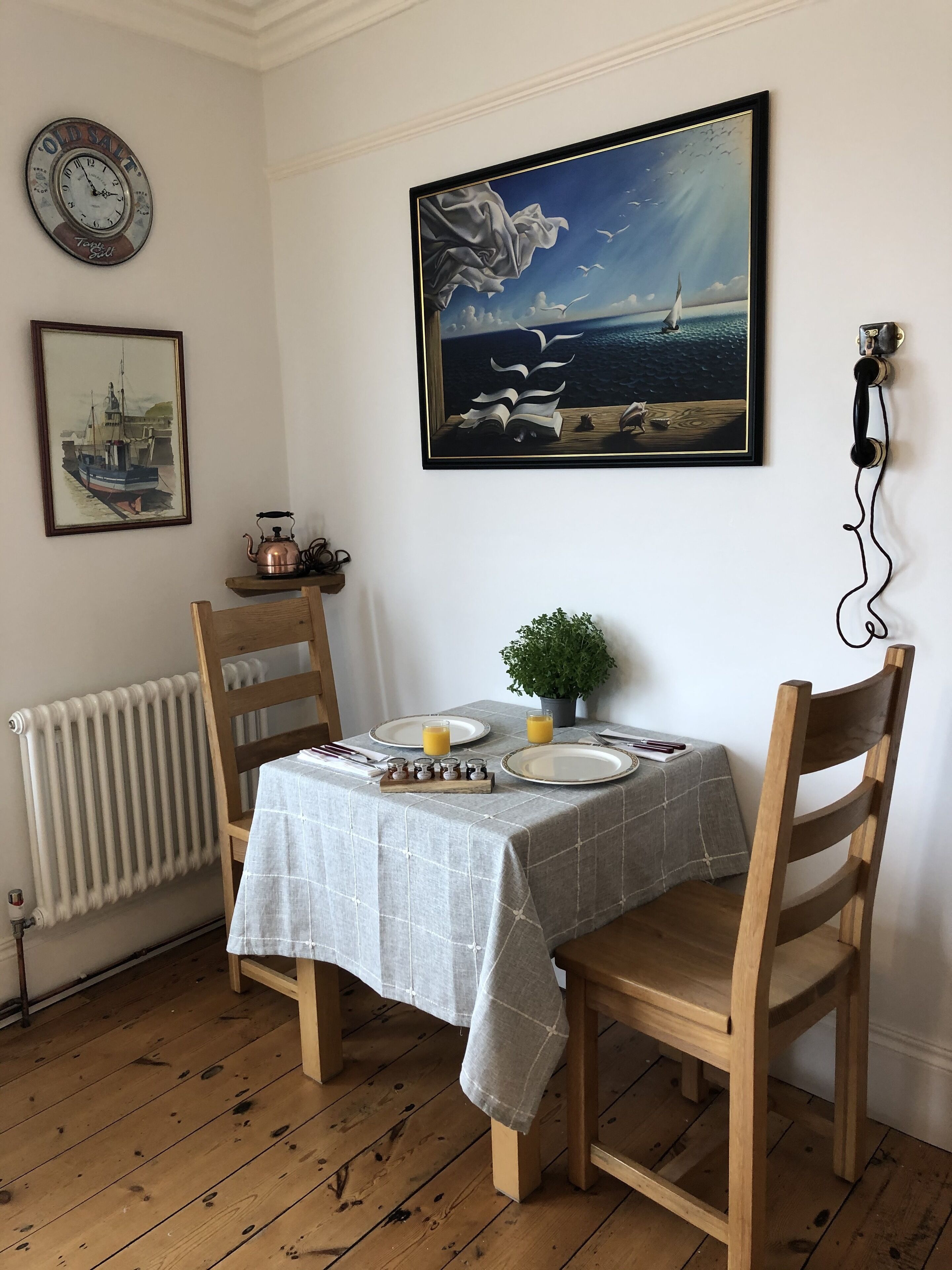 Un comedor con una mesa dispuesta para dos, un reloj y un cuadro en la pared.