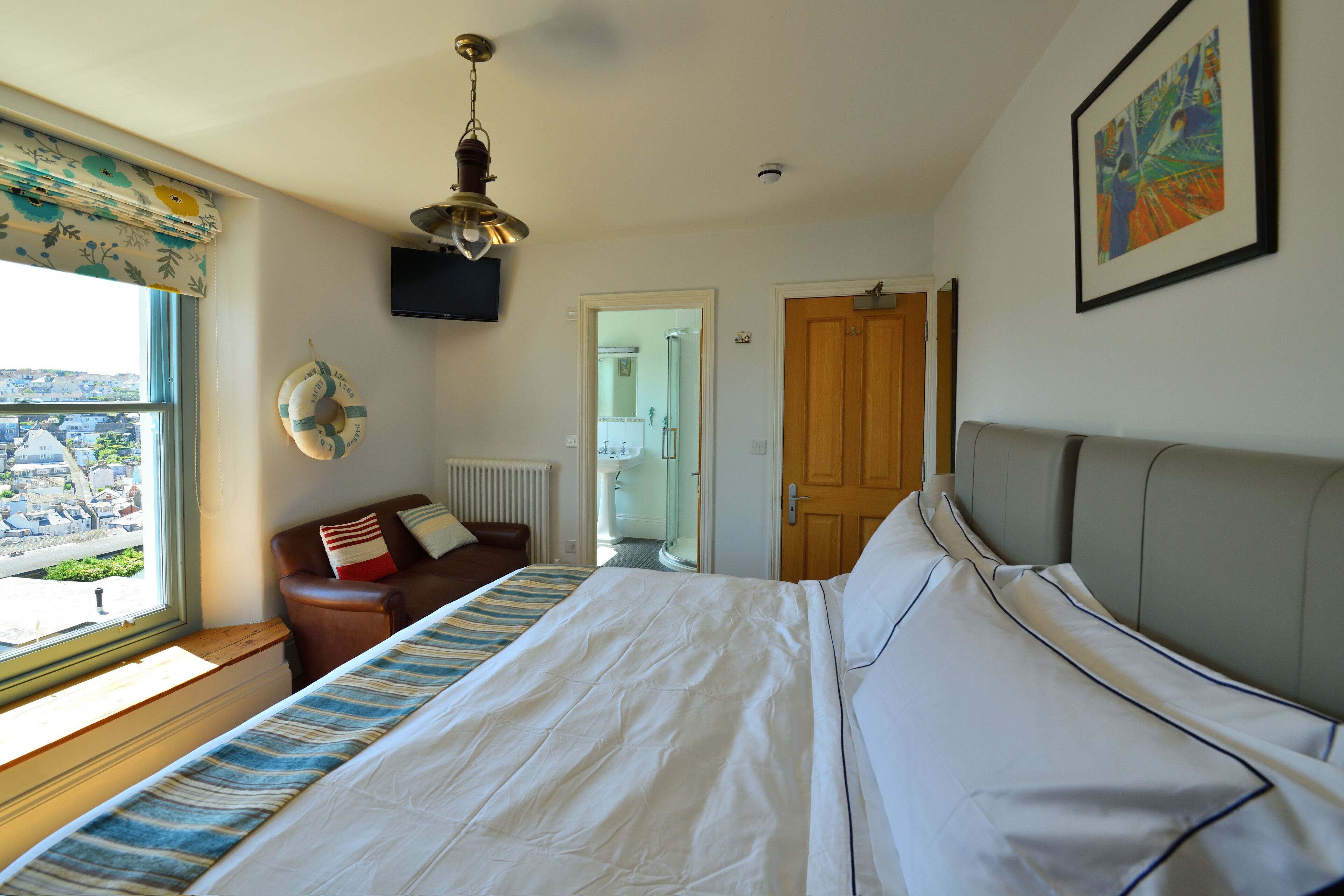 A hotel room with a large bed, a window with a view, a wooden door, and a ceiling fan.