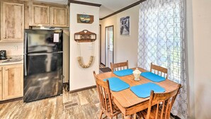 A compact kitchen with wooden cabinets, a black refrigerator, and a dining area with a wooden table and blue placemats. - 'Pelican Place' Coastal Cottage Walk to Back Sound (Harkers Island)