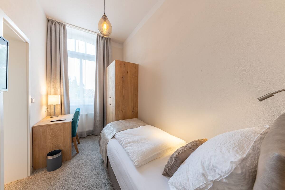 A bedroom with a bed, a desk, a chair, and a window with curtains.