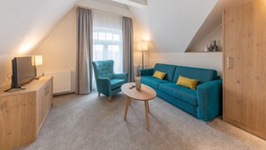 Una sala de estar moderna con un sofá azul, una mesita redonda, un sillón azul, un televisor y una lámpara.
