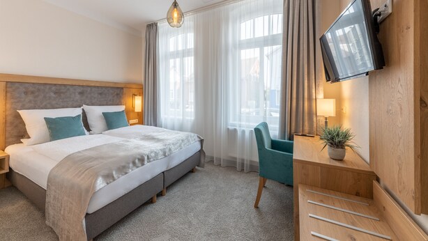 Una habitación de hotel con cama, escritorio con silla, televisión y ventana con cortinas.