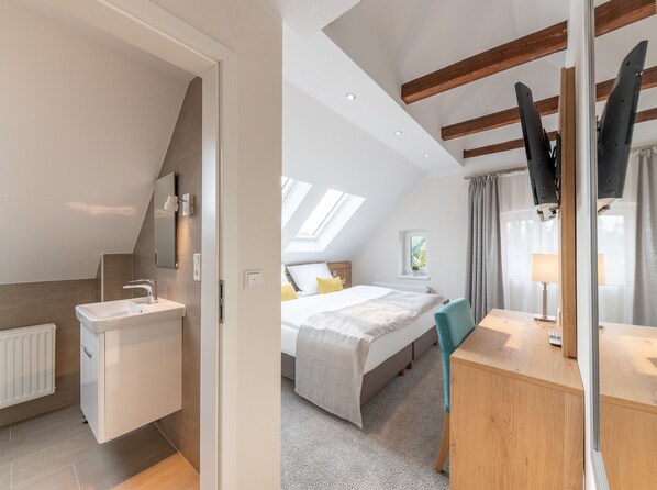 A modern bedroom with a skylight, a bed, a desk, and a bathroom with a sink and mirror.